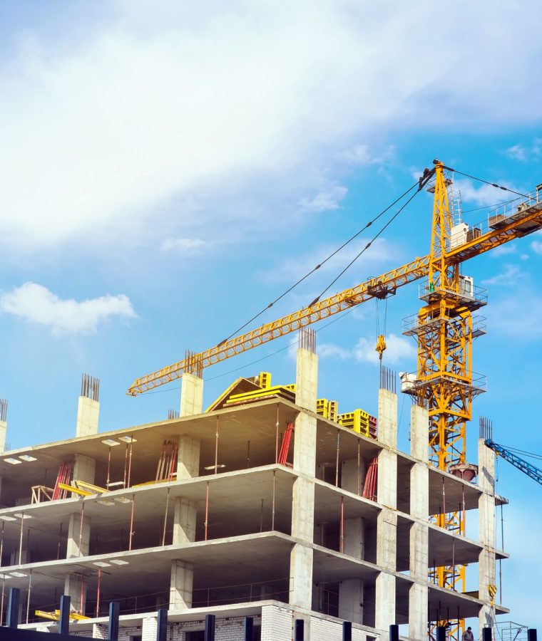 High yellow crane building a house in the beautiful bright blue sky with clouds. Workers in the building under construction is building a house.
